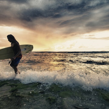 Surfer exiting water with surfboard at sunset in Rincon, Puerto Rico